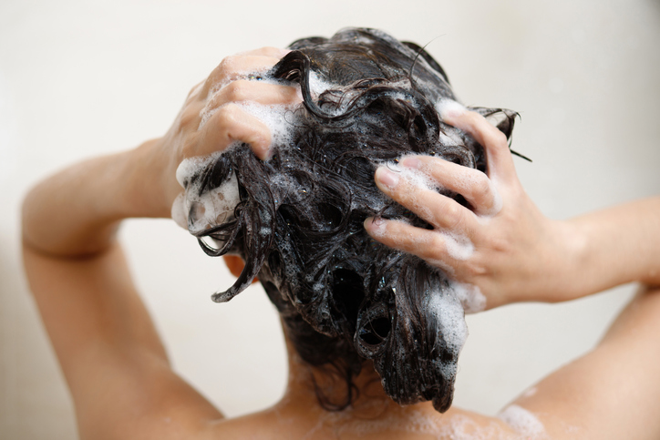 Woman taking shower and washing hair with shampoo in bathroom at home