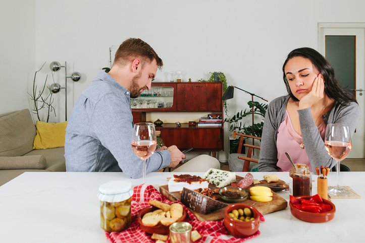 concept of phubbing in couple relationship - bored wife having aperitif with husband - distracted man snubbing woman - boring date