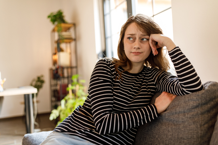 Distraught young woman sitting with head in hand, worrying and contemplating