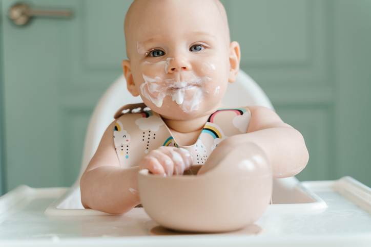 Pretty food-stained baby aged half a year eats yogurt sitting