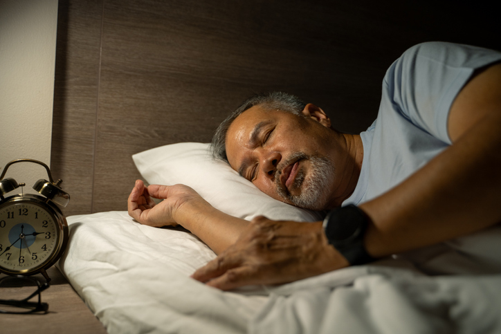 An elderly man wears a smartwatch on his arm to measure his sleep.
