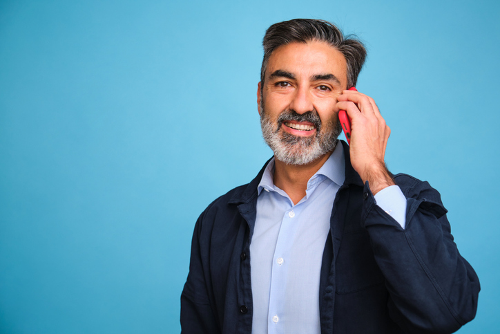 A man with a beard and gray hair is talking on a cell phone.