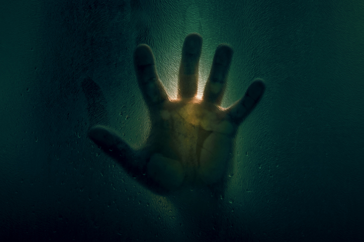 Horror scene of a man against wet glass. Hand against the background of a wet glass bathroom wall. Toned image. Horror concept