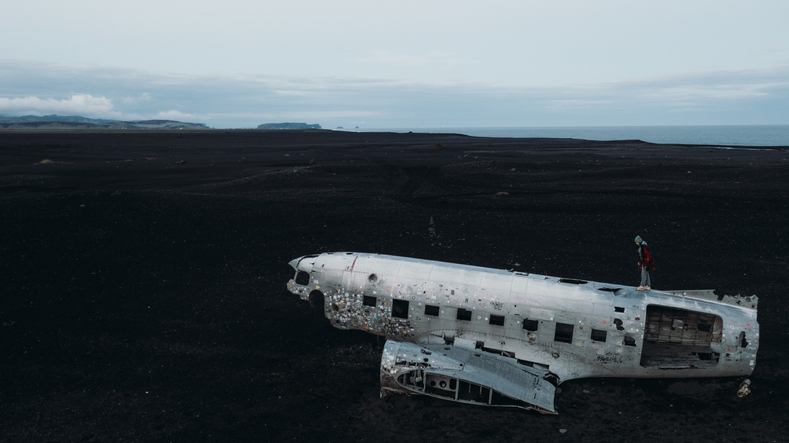 Woman in Red Admiring Black Volcanic Landscape Overlooking From Wrecked Plane in Iceland