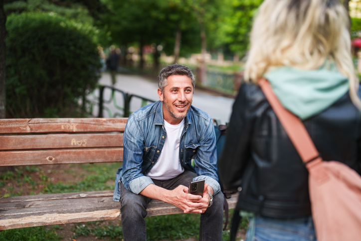 Man sitting on a bench, woman talking to man.