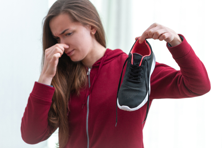 Woman is feeling unpleasant smell from sweaty running shoes after long sport training and active lifestyle. Footwear needs in cleaning and odor removal. Shoe care and shine