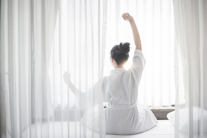 Rear View Of Woman Stretching Hands While Sitting On Bed At Home