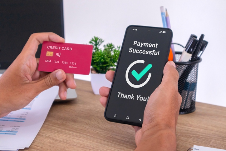 Hand holding credit card and using smartphone to make online payment. Successful payment message on smartphone screen.