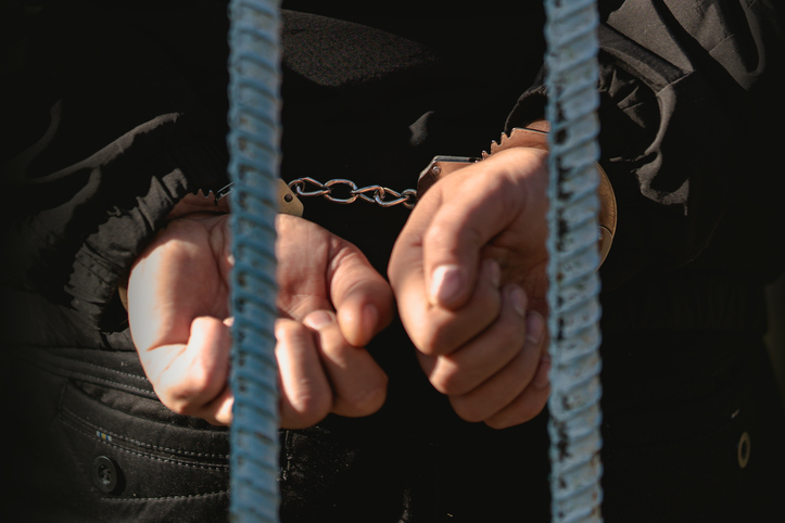 The man in the handcuffs is behind the bar in the police station. He was imprisoned. prisoner concept - picture