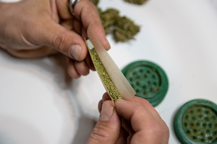 Rolling a joint with a weed bong to grind cannabis buds into the bottom.