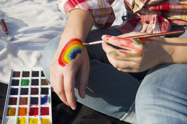 Close-up of the artist's hands holds a brush and draw LGBTQ flag rainbow.