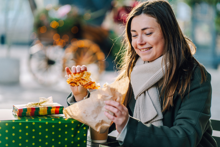Woman eating street food at Christmas market, enjoying festive atmosphere