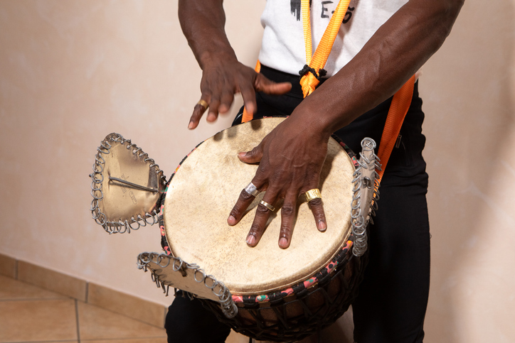 Musician playing talking drum with metal rings and orange straps