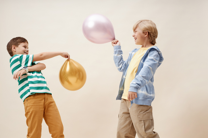 Two Young Male Friends Playing with Balloons on Neutral Background in Studio