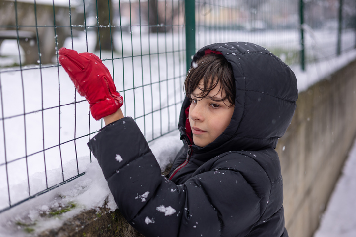Child in red mittens exploring snowy yard on winter day.