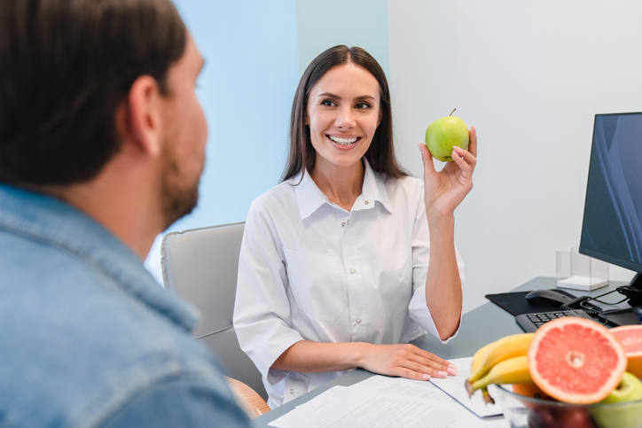 Doctor dietician giving advices to fat overweight patient. Female nutritionist doctor holding fresh fruits. Food choice, healthy and unhealthy food. Diet decision, healthy lifestyle and weight loss.