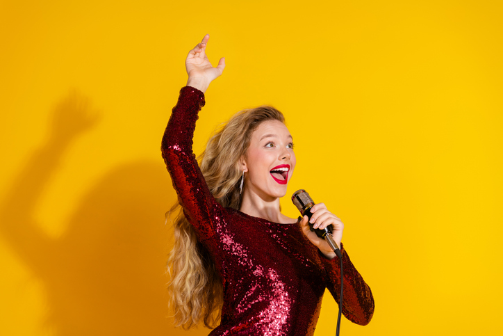 Charming woman singing in red sequined dress against bright yellow background, radiating celebration and glamour