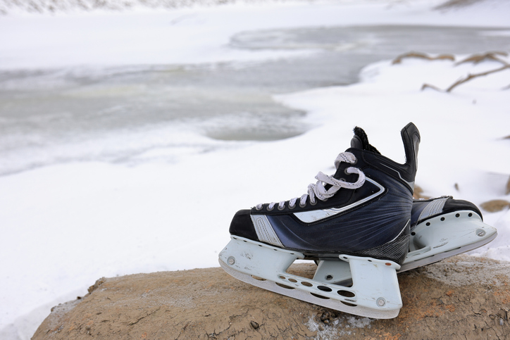 Hockey skates ready for outdoor pond hockey, with ice and snow in the background.