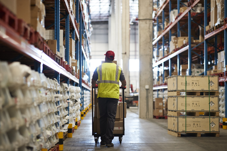 Rear view of warehouse worker walking with push cart