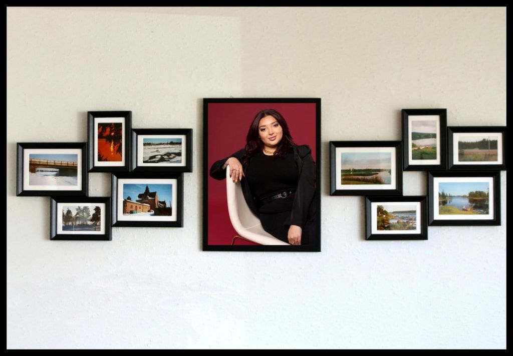 A gallery wall with framed landscape photos and a central portrait of a young woman in a black top posing against a red background.