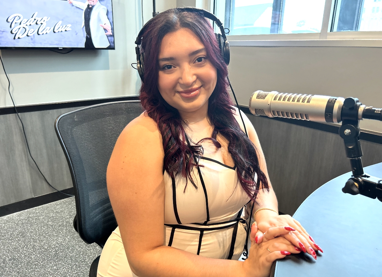 A smiling woman with long dark hair wearing headphones and sitting in a studio setting.
