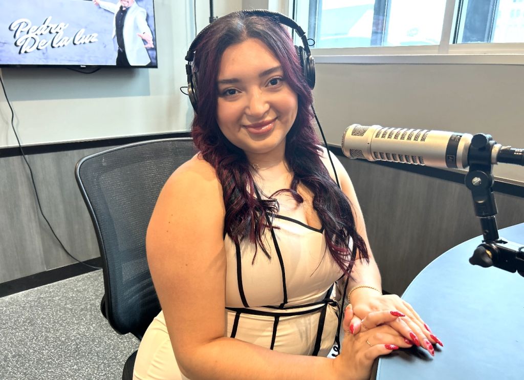 A smiling woman with long dark hair wearing headphones and sitting in a studio setting.