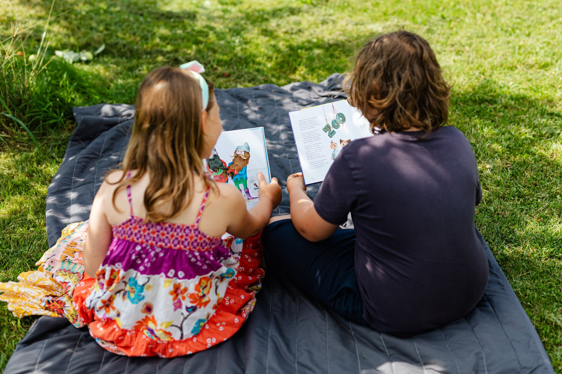 children reading books while sitting on blue blanket on green grass