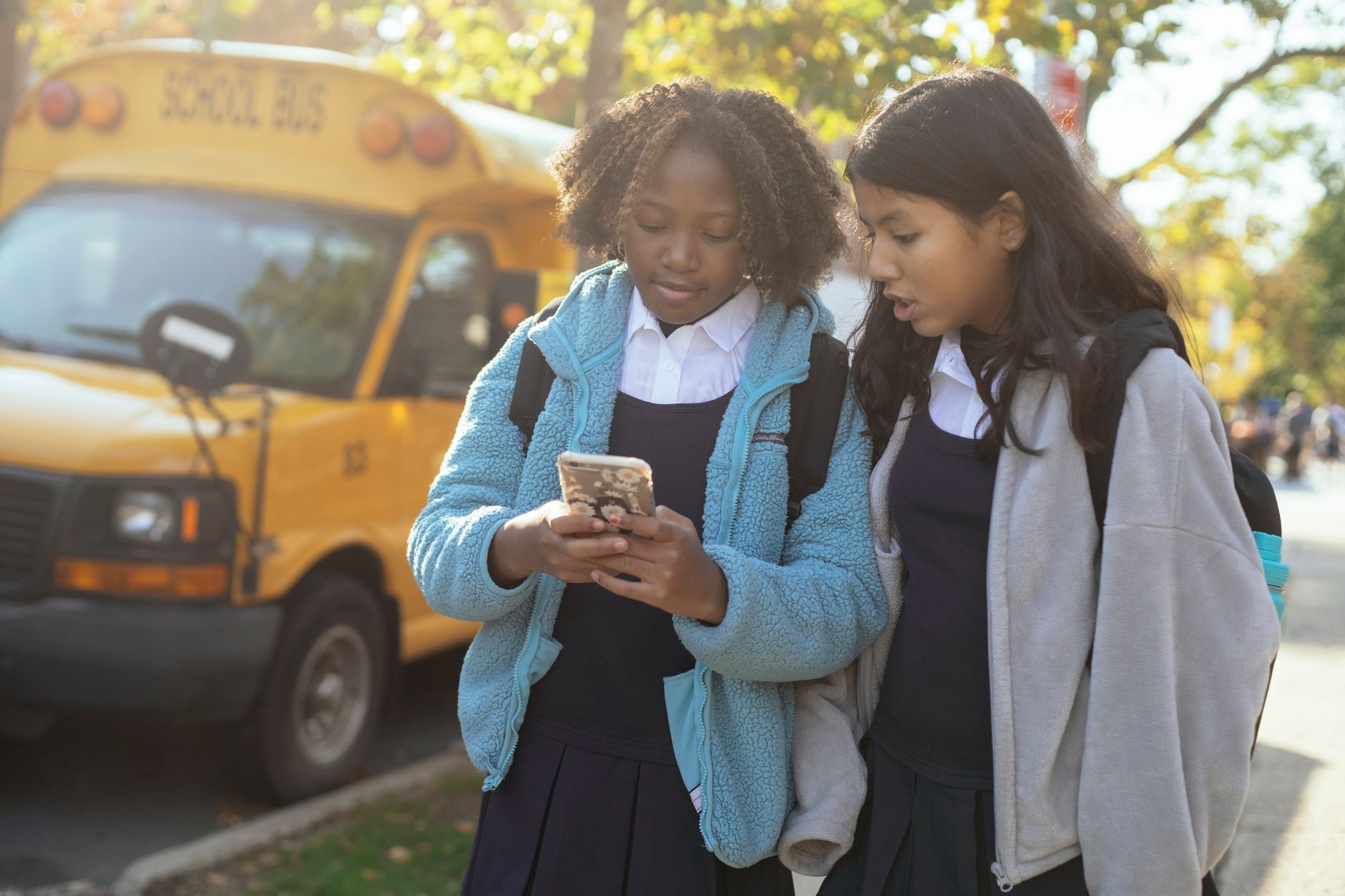 diverse schoolgirls surfing smartphone on sunny street