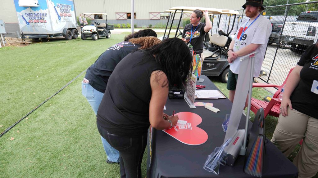 People at a booth setting up and decorating with a large red heart-shaped sign.
