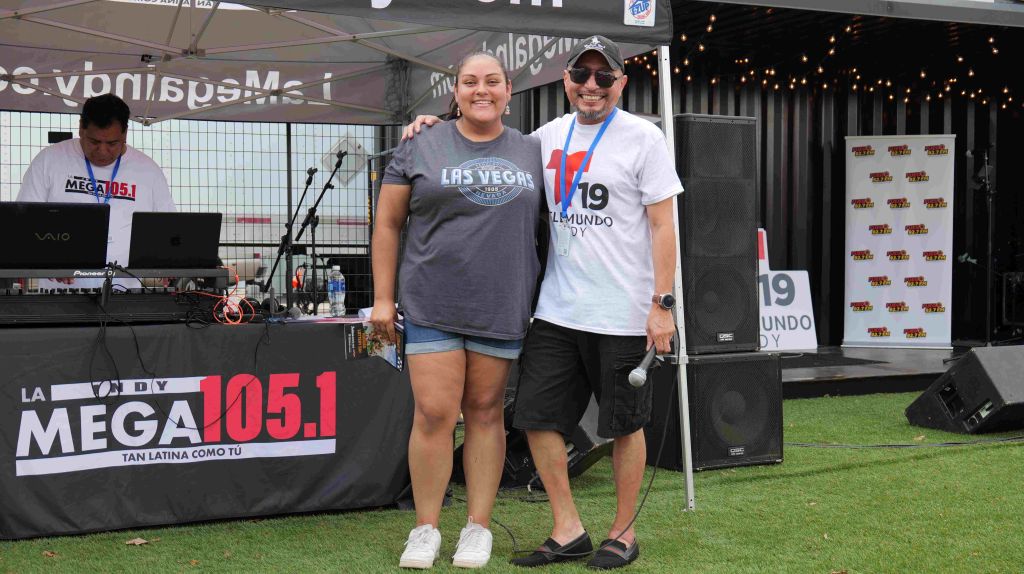 Two people standing in front of a radio station booth with "La Mega 105.1" branding, one wearing a "Las Vegas" t-shirt and the other a "19 Undo" t-shirt.